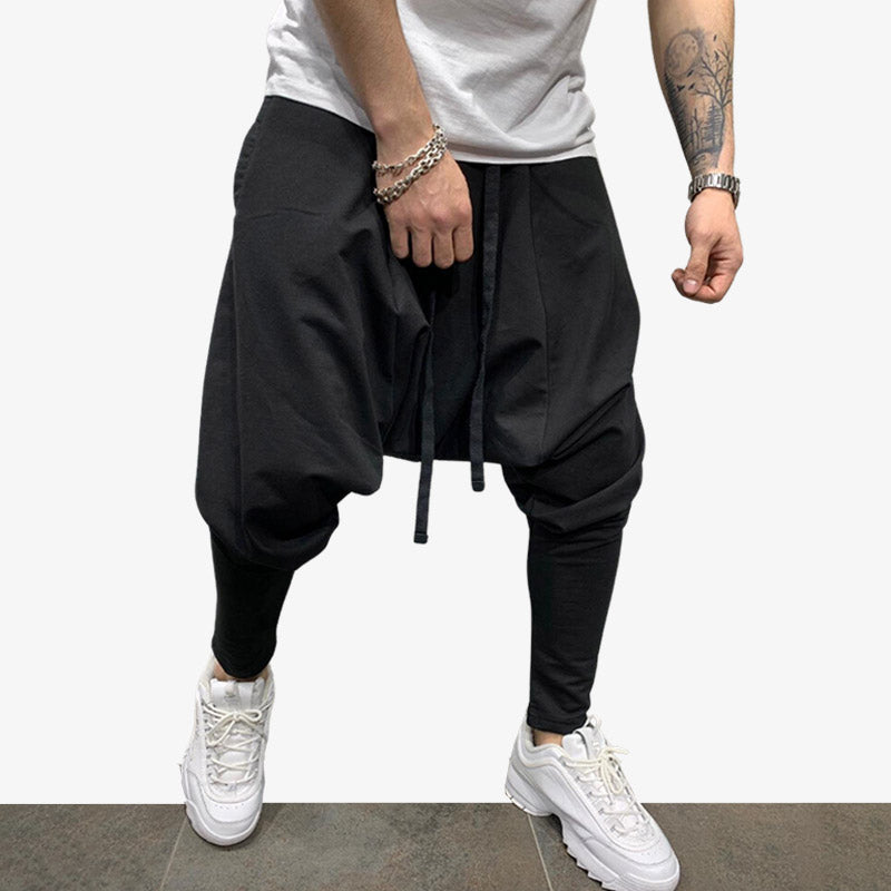 Un homme est debout avec un pantalon japonais street style. Il porte aussi un t-shirt blanc et des sneakers blanches
