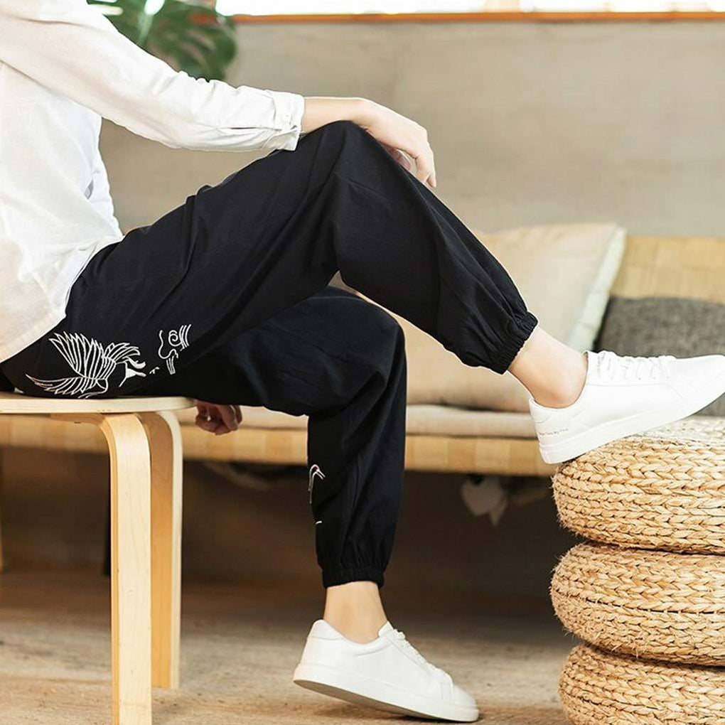 Pantalon streetwear japonais zen aux motifs blancs, assis sur un tabouret en bois