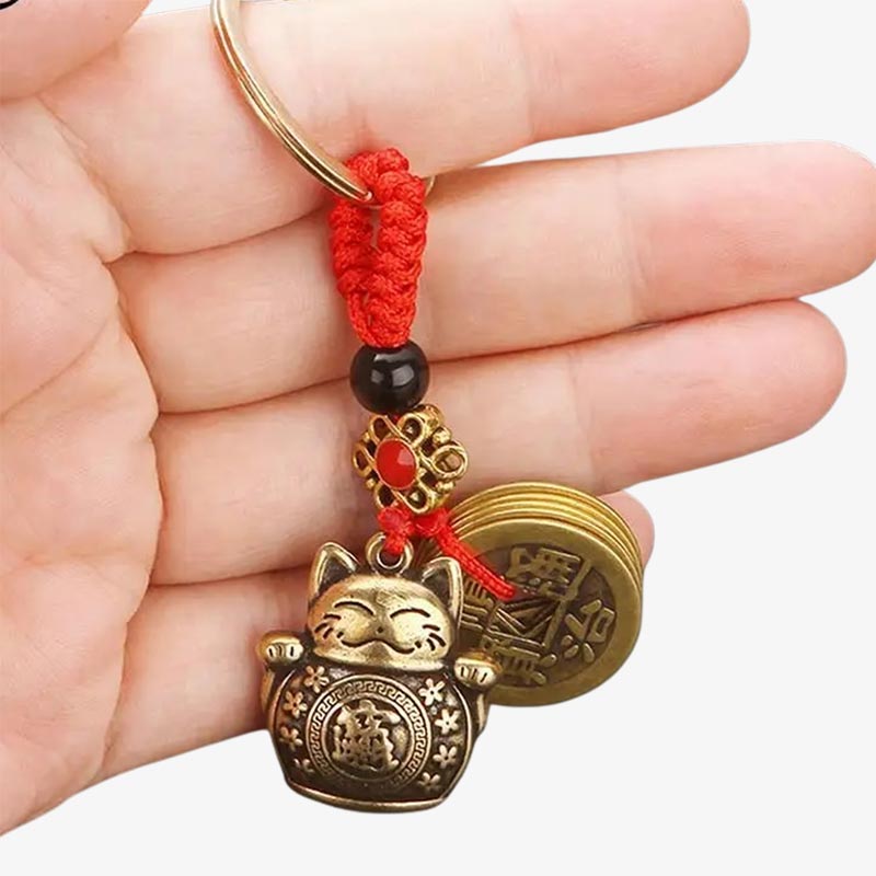 Une personne tien dans la maint un porte clé chat japonais avec des pièces de monnaies