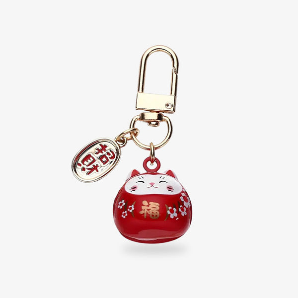 porte-clé maneki neko kawaii de couleur rouge et en forme de chat japonais. L'objet est peint avec des symboles de fleurs de sakura et un kanji doré. La piècette est gravée avec un kani signifiant en japonais : invitaiton à la richesse