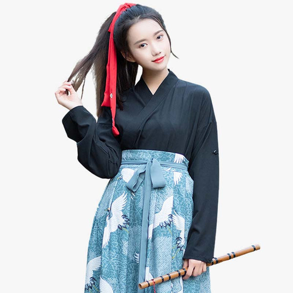 Une femme est habillé avec une robe Hakama aux motif japonais Tsuru (grue) imprimés sur le tissu. Elle se tient les cheveux et est habillé avec un haut de kimono noir