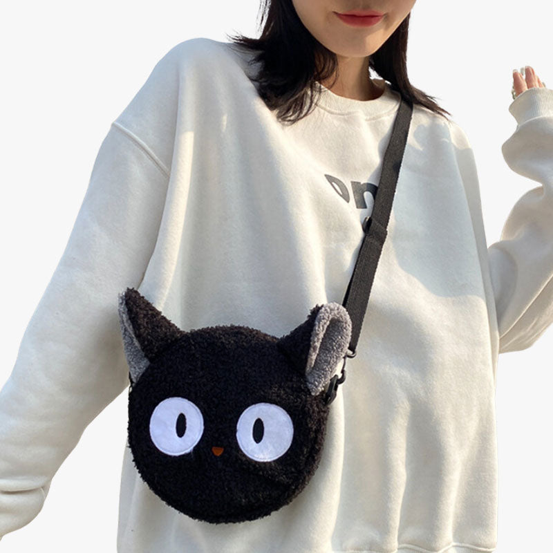 Une femme porte un sac kawaii noir en forme de tete de chat noir avec des grands yeux. C'est un sac bandoulière en matière douce.