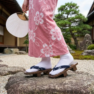 Geta motif kanji portées avec un kimono rose dans un jardin japonais