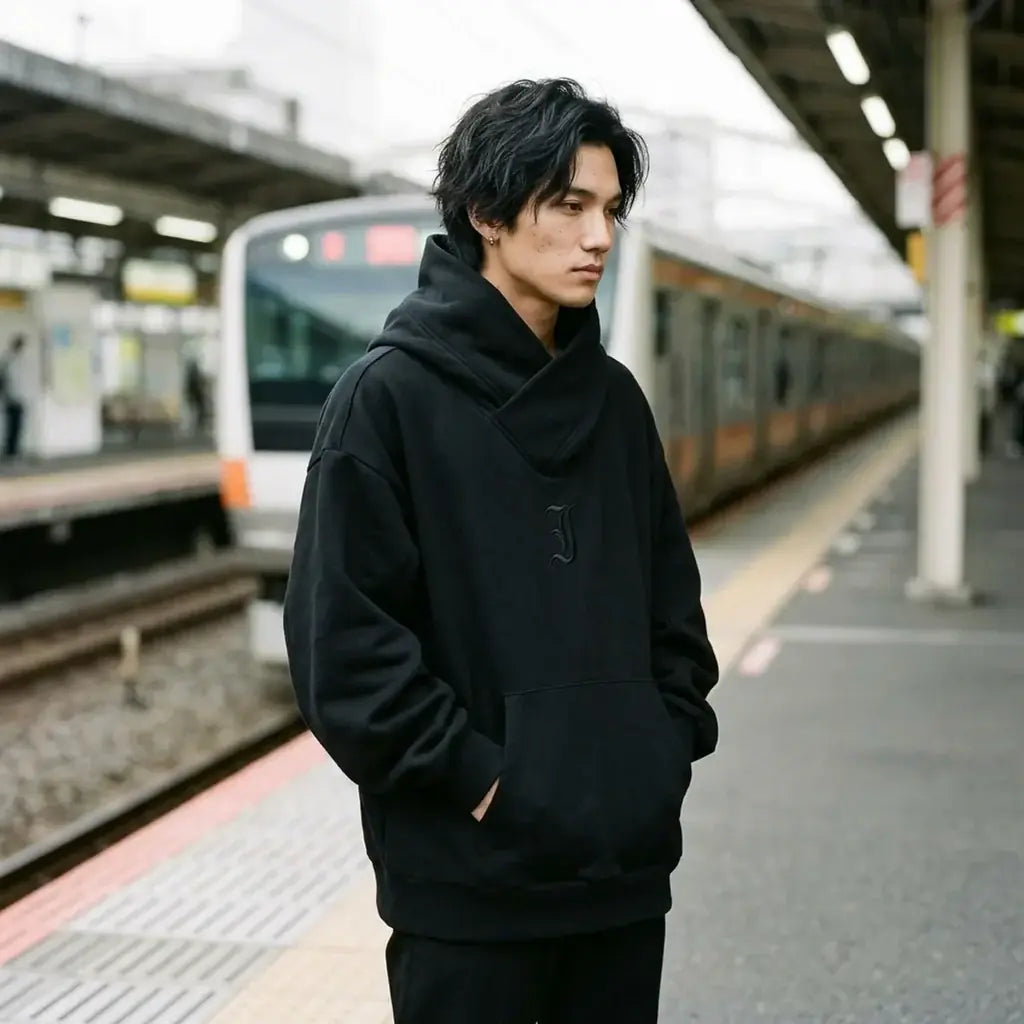 Hoodie noir streetwear japonais porté sur un quai de train extérieur à Tokyo sous un ciel couvert