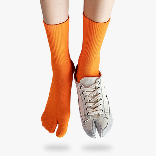 Une paire de tabi chaussettes avec le bout fendu et de couleur orange. Une paire de chaussures blanche avec un doigt sur la jambe droite