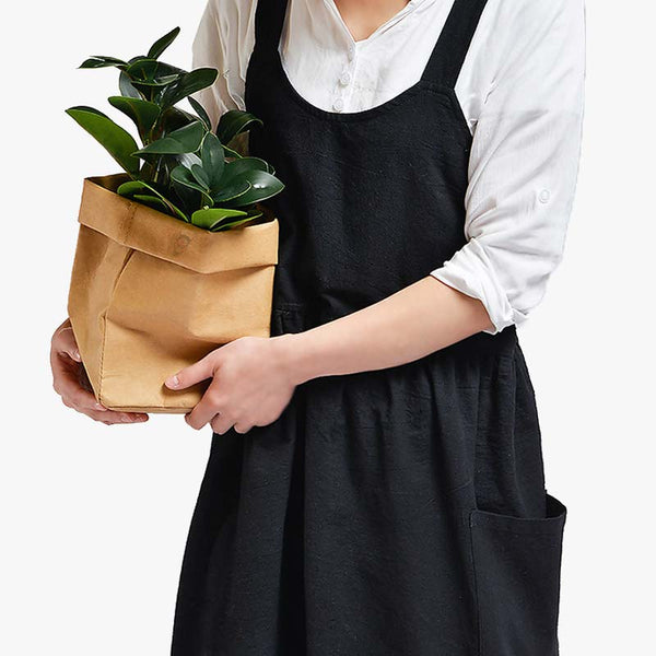 Une femme est habillée avec un tablier en lin japonais  de couleur noir et une chemise blanche. Elle porte dans la main des Fleurs. Le tablier de jardinage protège des taches de cuisine et du jardin