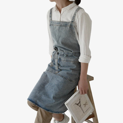 Tablier japonais femme en denim bleu robuste, bretelles croisées pour le confort et poche avant pratique, idéal pour la cuisine et les travaux créatifs.