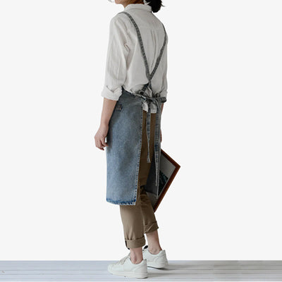 Tablier de travail japonais en denim bleu, conçu avec bretelles croisées et poche avant, offrant protection durable et style pour la cuisine et l'atelier.
