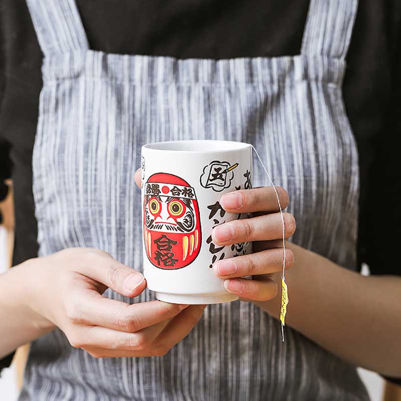 une gemme tient dans les mains une tasse a the japonais daruma