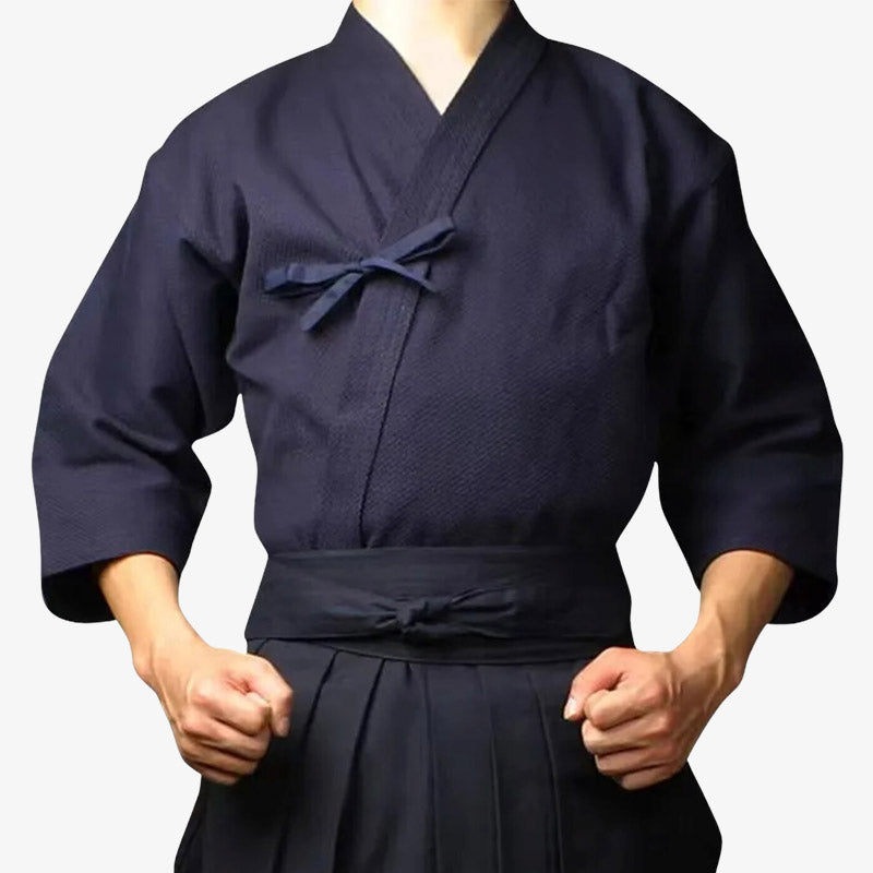 Un homme est haibillé avec une tenue aikido qui se compose d'un keikogi bleu marine et d'un hakama noir