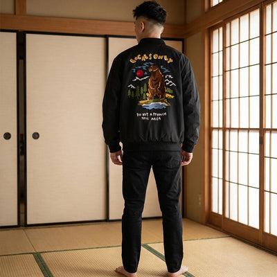 Personne portant un blouson bomber traditionnel japonais noir orné d'un ours brodé, dans une pièce aux tatamis et portes shoji