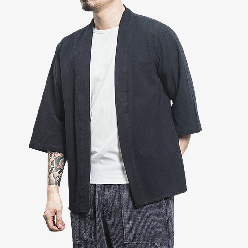 Un homme japonais est habillé avec une veste kimono cardigan qui se porte sans ceinture et ouverte. C'est un vêtement japonais homme en lin et en coton. La couleur de la veste haori est noire