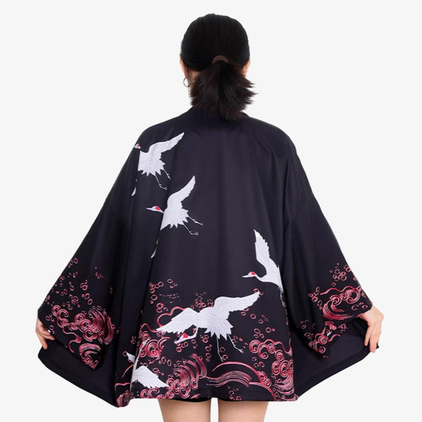 Une femme est habillée avec une veste kimono tsuru. C'est une veste haori de couleur avec des imprimés blancs de l'oiseau Tsuru