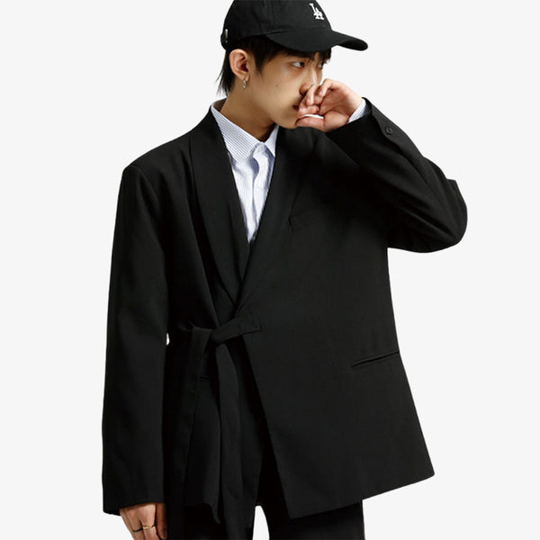 Un homme japonais avec une casquette est habillé avec une veste style kimono de couleur noire. Il porte aussune une chemise blanche. Le manteau kimono est fermé via une ceinture obi latérale en coton et de couleur noire