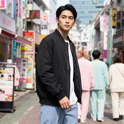 Homme portant une veste sukajan noire dans une rue animée de Harajuku, entourée d'enseignes colorées