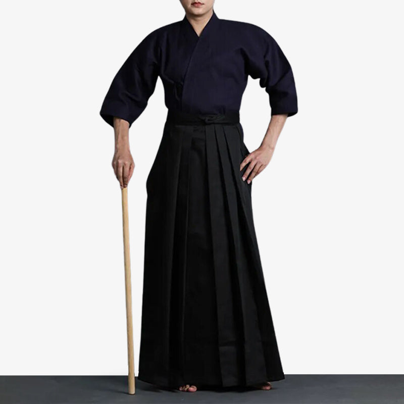 un homme est habillé avec un vêtement d'art martial japonais. Il a un pantalon hakama noir et un kimono d'entrainement de couleur bleu que l'on appelle un keikogi