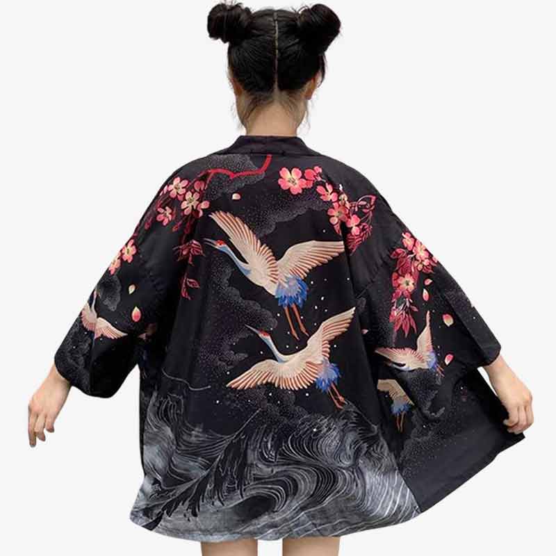 Femme japonaise portant un haori veste kimono noir avec des motifs japonais d'oiseaux grue et des fleurs de cerisiers sakura imprimées sur le tissu du haori femme