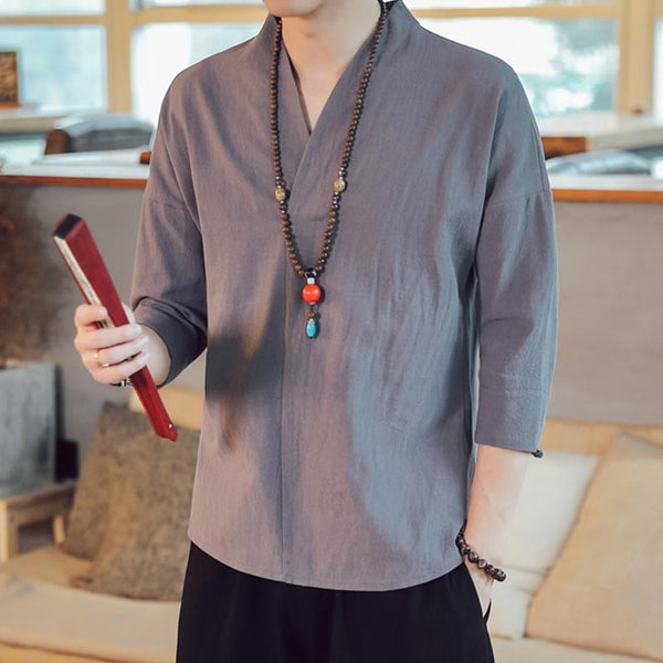 Un homme est vêtu avec un T-shirt japon de couleur gris. Il porte dans la main un accessoire japonais et un collier zen autour du cou
