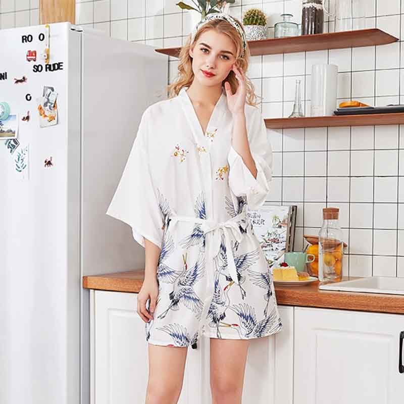 Une femme porte une chemise de nuit kimono dans une cuisine. Vêtement japonais avec des motifs d'oiseaux brodés sur le tissu en satin