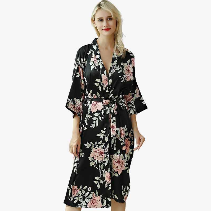 Un femme porte un kimono long pyjama noir avec des motifs fleurs imprimés sur le tissu