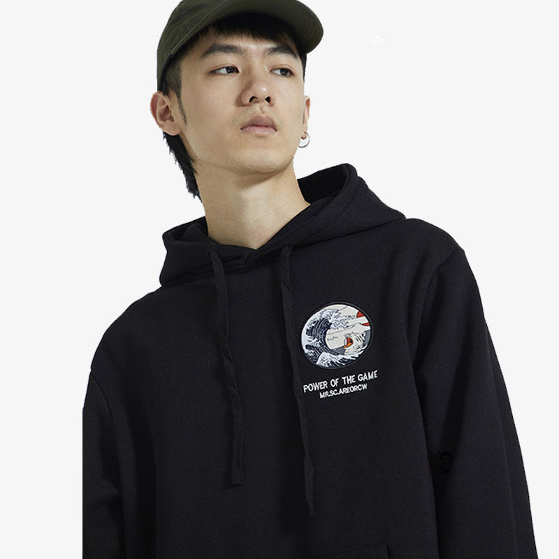 Un homme porte un sweat vague japonaise et une casquette. Un patch est brodé sur le coton