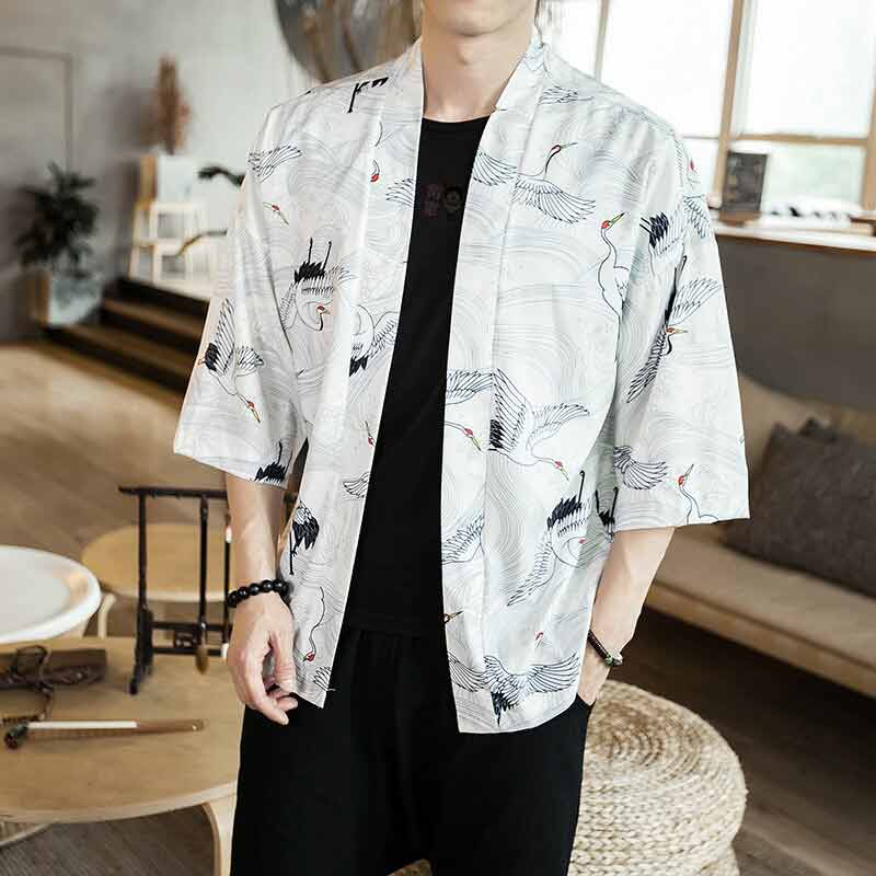 Un homme porte une veste effet kimono blanc avec des oiseaux imprimés sur le tissus. Il porta une t-shirt noir et un pantalon cargo noir