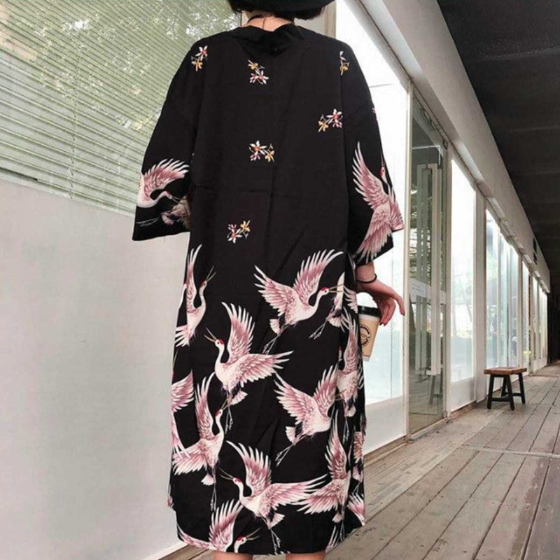 Une femme porte une veste kimono long avec des oiseaux grues imprimés sur le dos du tissus noir en coton
